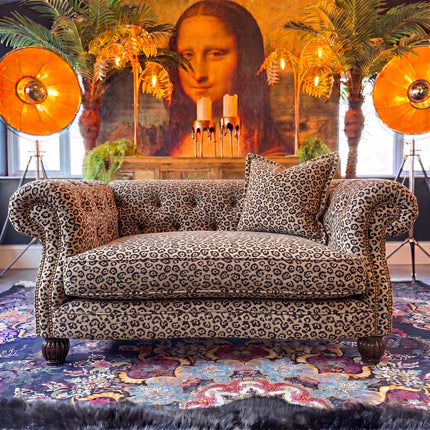 Patterned sofa with decorative pillows in a room with palm trees and large windows.